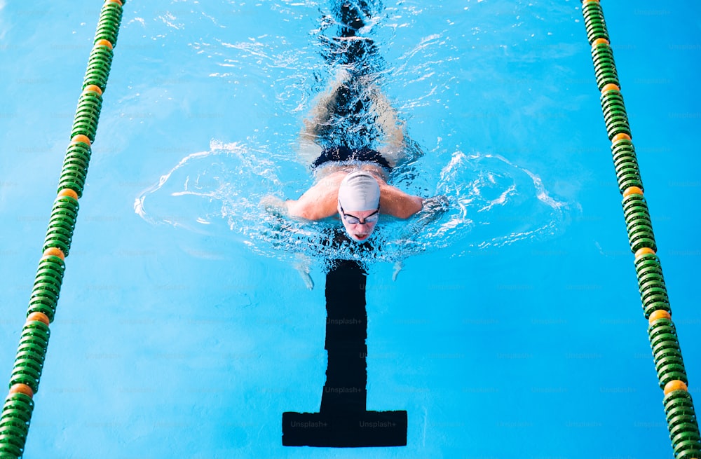 Senior man swimming in an indoor swimming pool. Active pensioner enjoying sport.