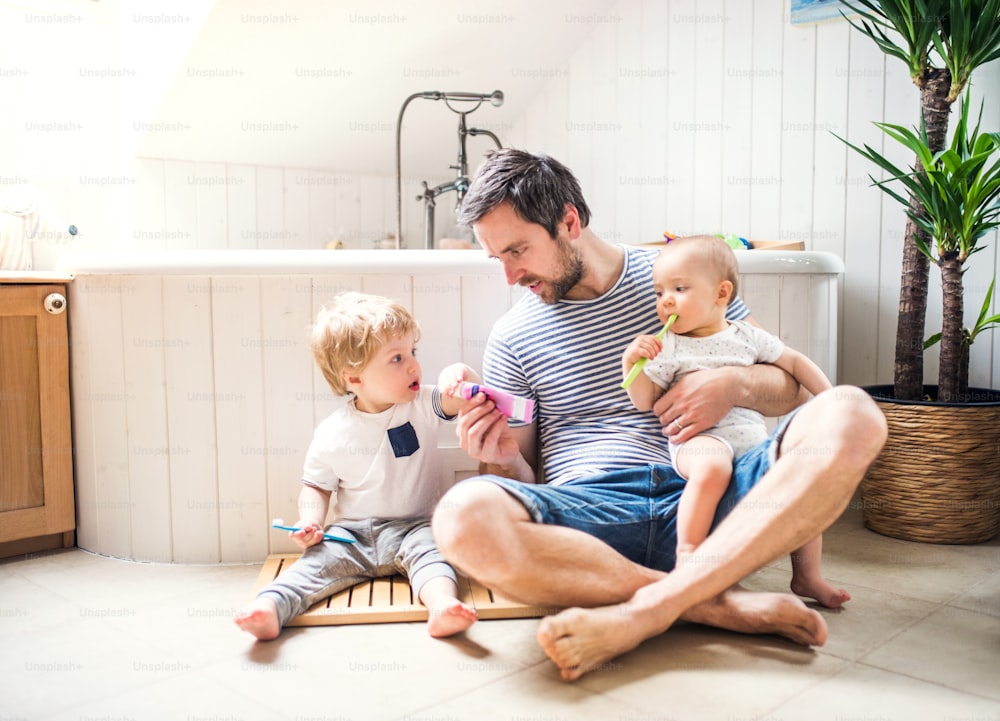 Padre con due bambini piccoli che si lava i denti nel bagno di casa. Congedo di paternità.