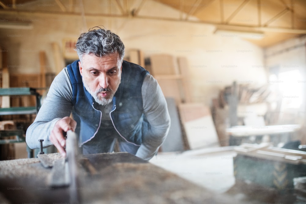 Um trabalhador maduro na oficina de carpintaria, trabalhando com madeira.
