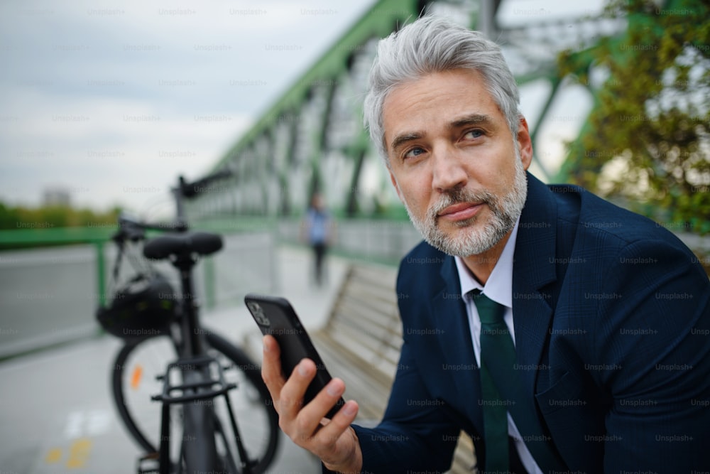 Ein Geschäftsmann mit Fahrrad sitzt auf der Bank, mit Smartphone. Pendler- und alternatives Verkehrskonzept