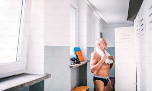 Älterer Mann steht an den Schließfächern in einem Hallenbad. Aktiver Rentner mit Spaß am Sport.