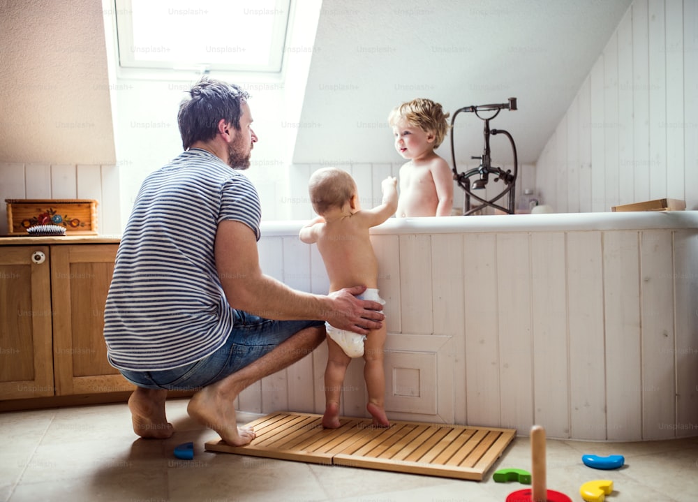 Vater wäscht zwei Kleinkinder in der Badewanne im Badezimmer zu Hause. Vaterschaftsurlaub.