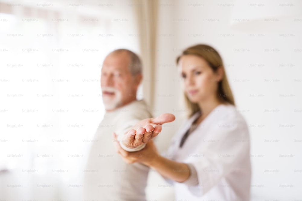 Health visitor and a senior man during home visit. A nurse or a physiotherapist helping a senior man exercise.