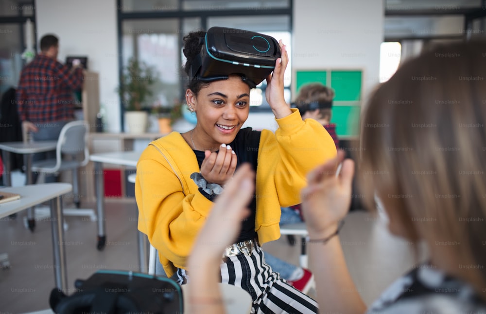 Una estudiante feliz con gafas de realidad virtual en la escuela en la clase de informática, jugando con su compañera de escuela.