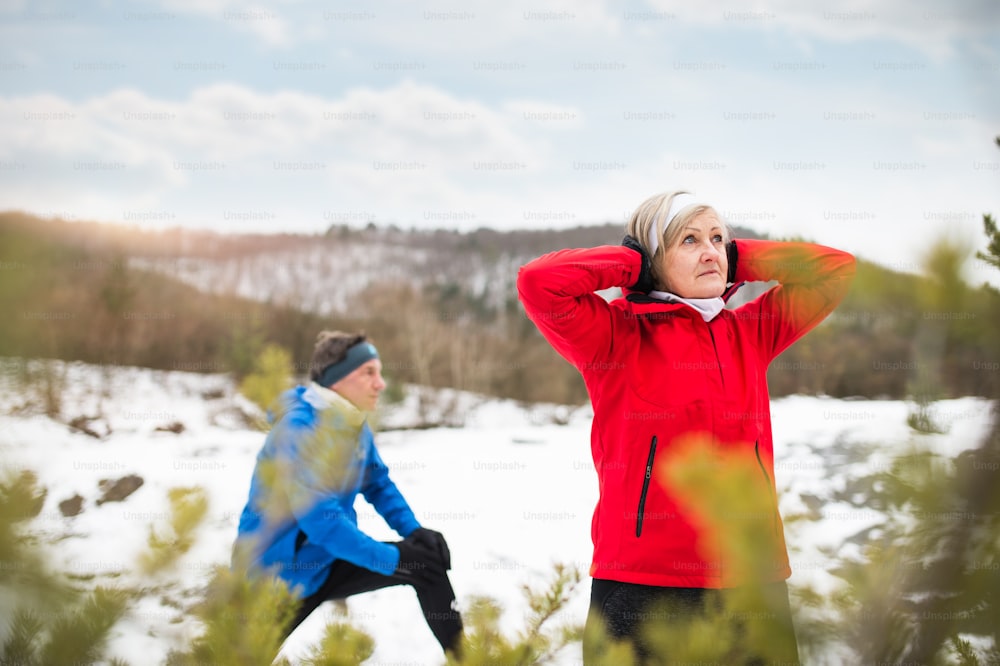 冬の自然の中で外でジョギングし、ストレッチをするシニアカップル。