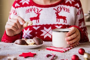 Composizione natalizia su sfondo in legno vintage. Donna irriconoscibile che mangia biscotti e beve caffè.