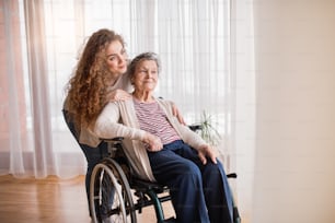 A teenage girl with grandmother in wheelchair at home. Family and generations concept.