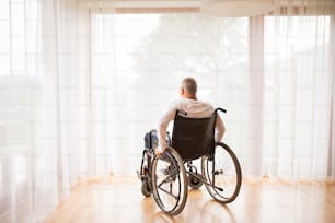 Homme âgé assis sur un fauteuil roulant à la maison. Vue arrière.