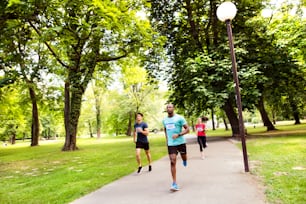 Group of young athletes running in green sunny summer park.