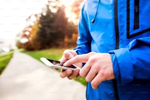 Unrecognizable runner outside in sunny autumn nature using a fitness app on his smartphone. Using phone app for tracking weight loss progress, running goal or summary of his run.
