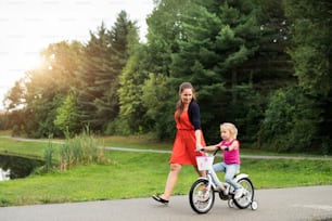 Young beautiful mother wiht her cute little daughter in nature, daughter is cycling and smilling. Slow motion.