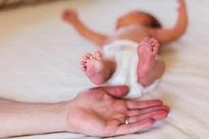 Unrecognizable young mother at home with her cute baby daughter lying on bed. Close up of legs and hand.