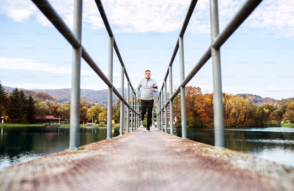 Junger Sportler mit Smartphone in grauer Jacke läuft draußen. Trailrunner-Training für Crosslauf in bunter sonniger Herbstnatur.