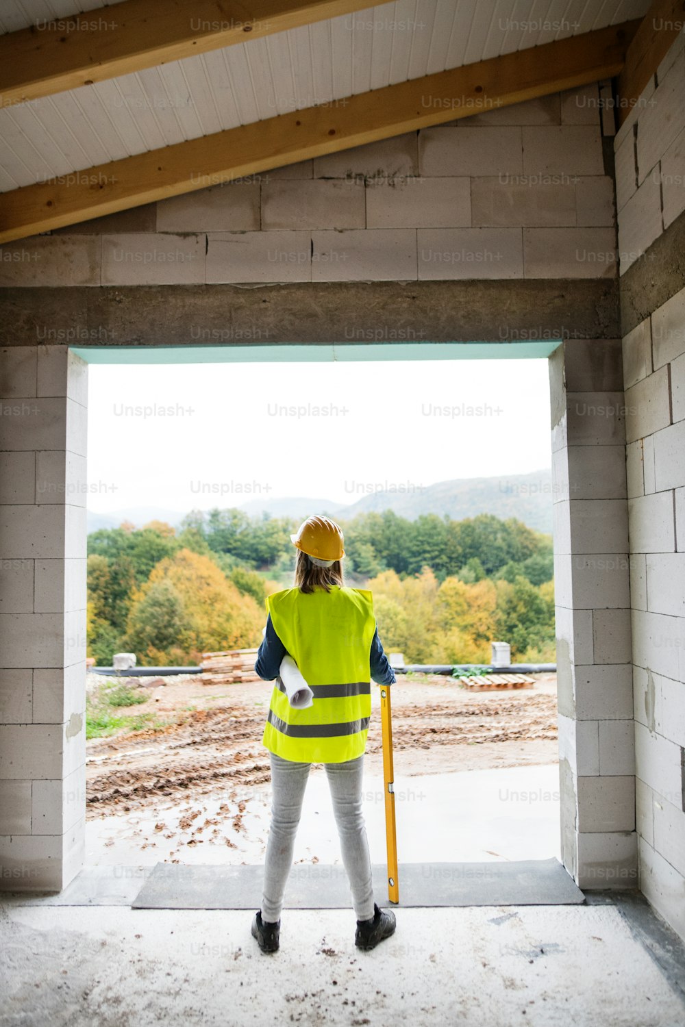 Female worker on the building site. Young woman holding blueprints. House construction. Rear view.