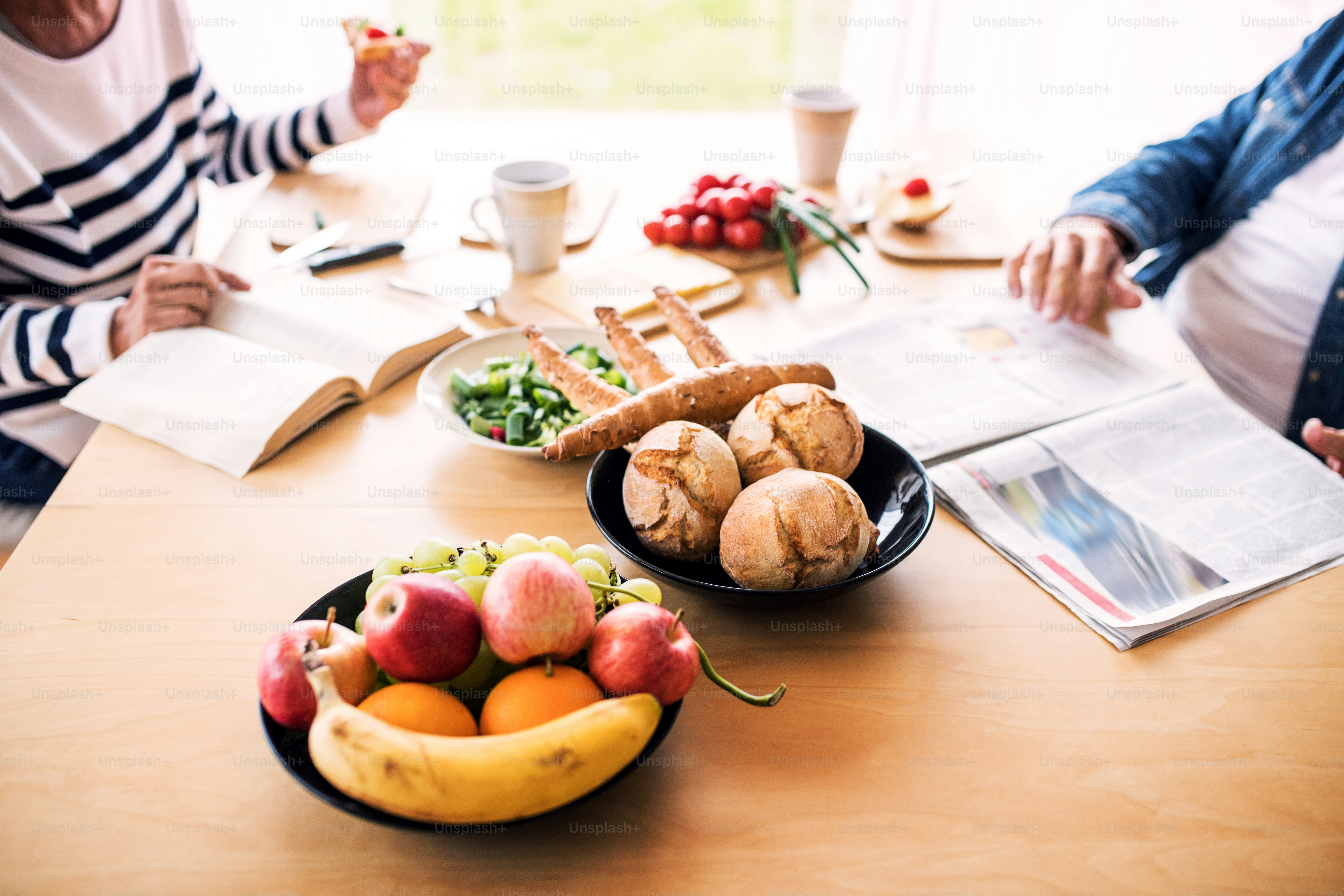 Pareja de ancianos irreconocible desayunando en casa. Un anciano y una anciana sentados a la mesa, leyendo.