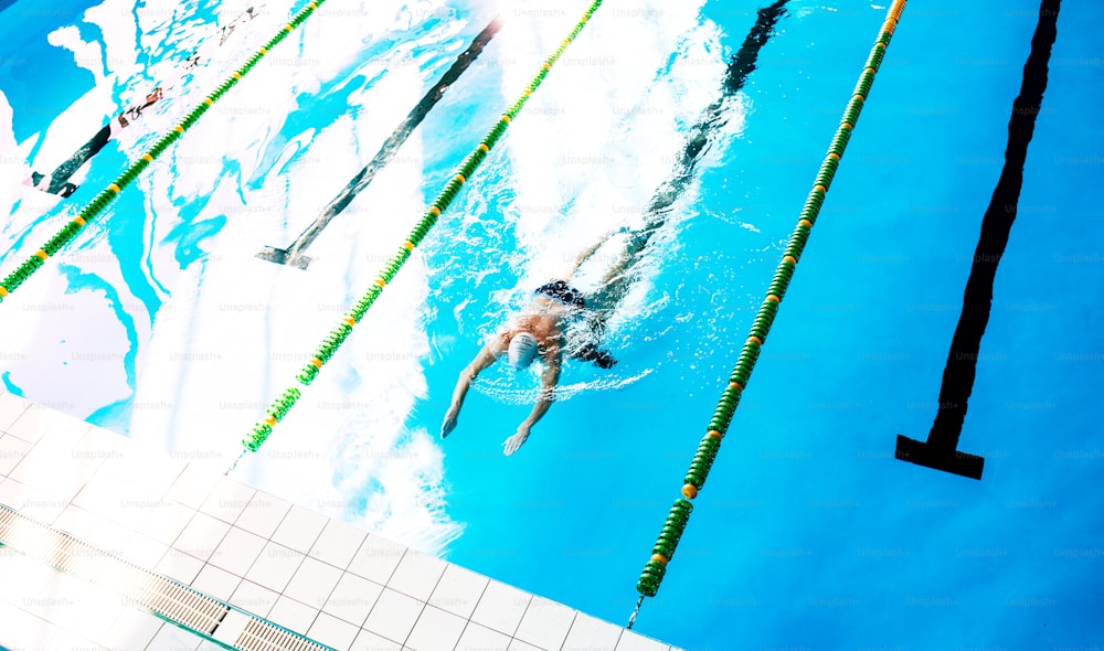 Hombre mayor nadando en una piscina cubierta. Jubilado activo disfrutando del deporte. Vista superior.