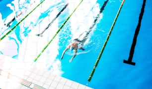 Homme âgé nageant dans une piscine intérieure. Retraité actif qui fait du sport. Vue de dessus.