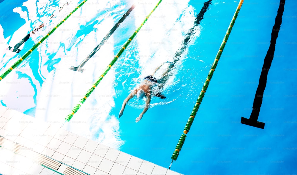 Senior man swimming in an indoor swimming pool. Active pensioner enjoying sport. Top view.