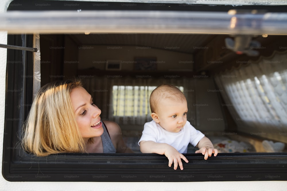 Beautiful young mother and her baby son in a camper van on a summer day.