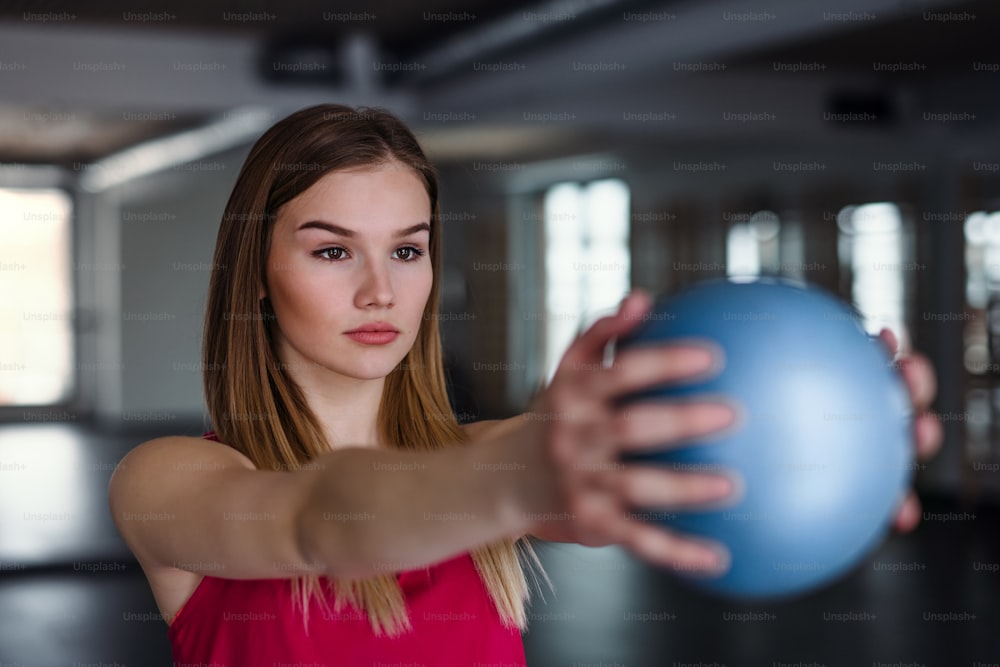 A portrait of a beautiful young girl or woman doing exercise with a ball in a gym.