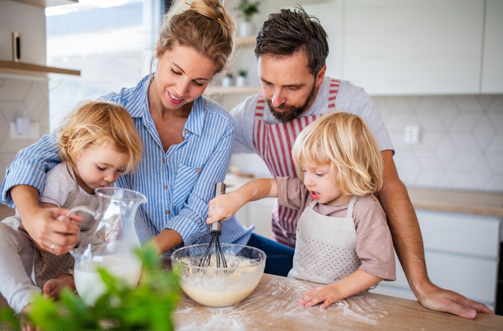 Una giovane famiglia con due bambini piccoli all'interno in cucina, cucinando.