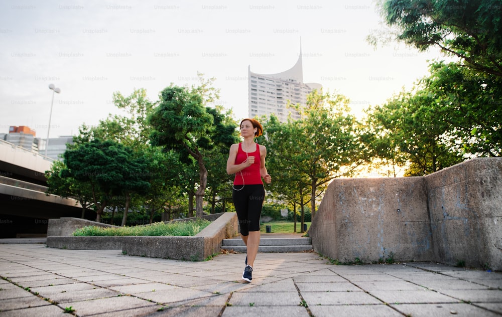 Young woman runner jogging outdoors in city at sunrise early in the morning.