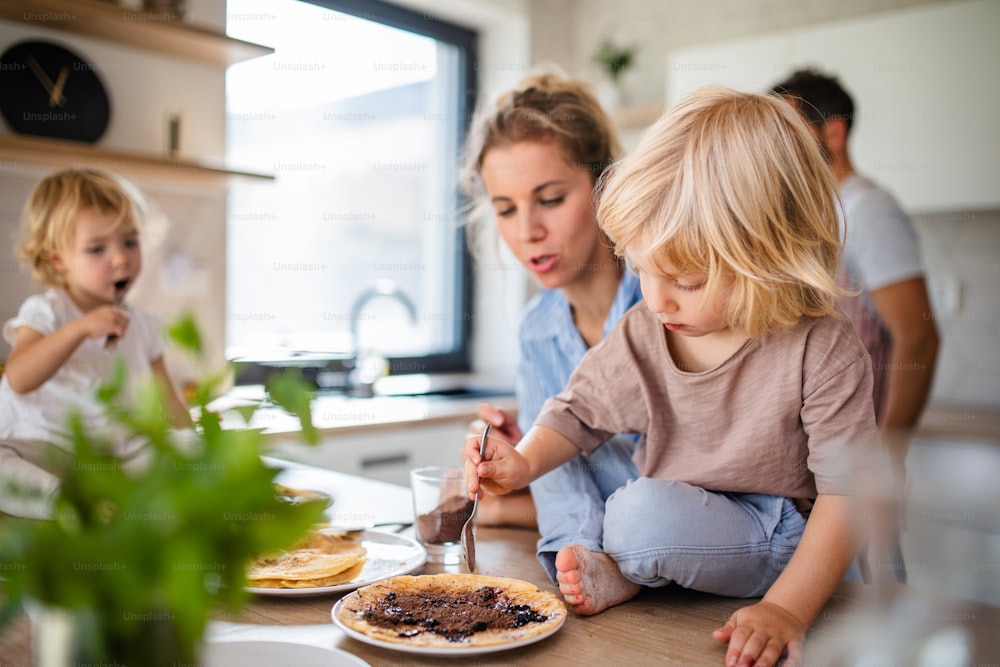 Una giovane famiglia con due bambini piccoli al chiuso in cucina, che mangia frittelle.