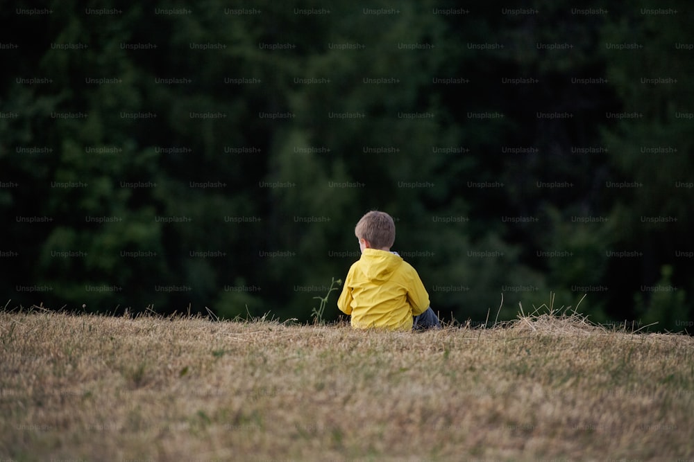 A rear view of school child sitting on field trip in nature, resting.