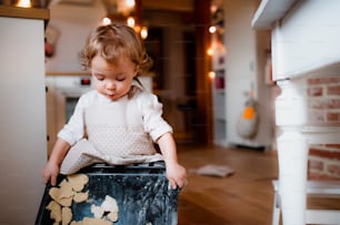 Una niña pequeña contenta haciendo pasteles en el suelo de la cocina de casa.