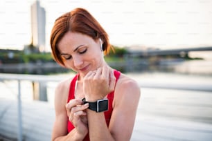 Giovane donna corridore con auricolari in città, usando lo smartwatch durante il riposo.
