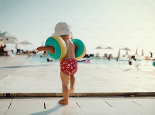 Eine Rückansicht eines kleinen Kindes mit Armbinden, das im Sommerurlaub am Strand spazieren geht.