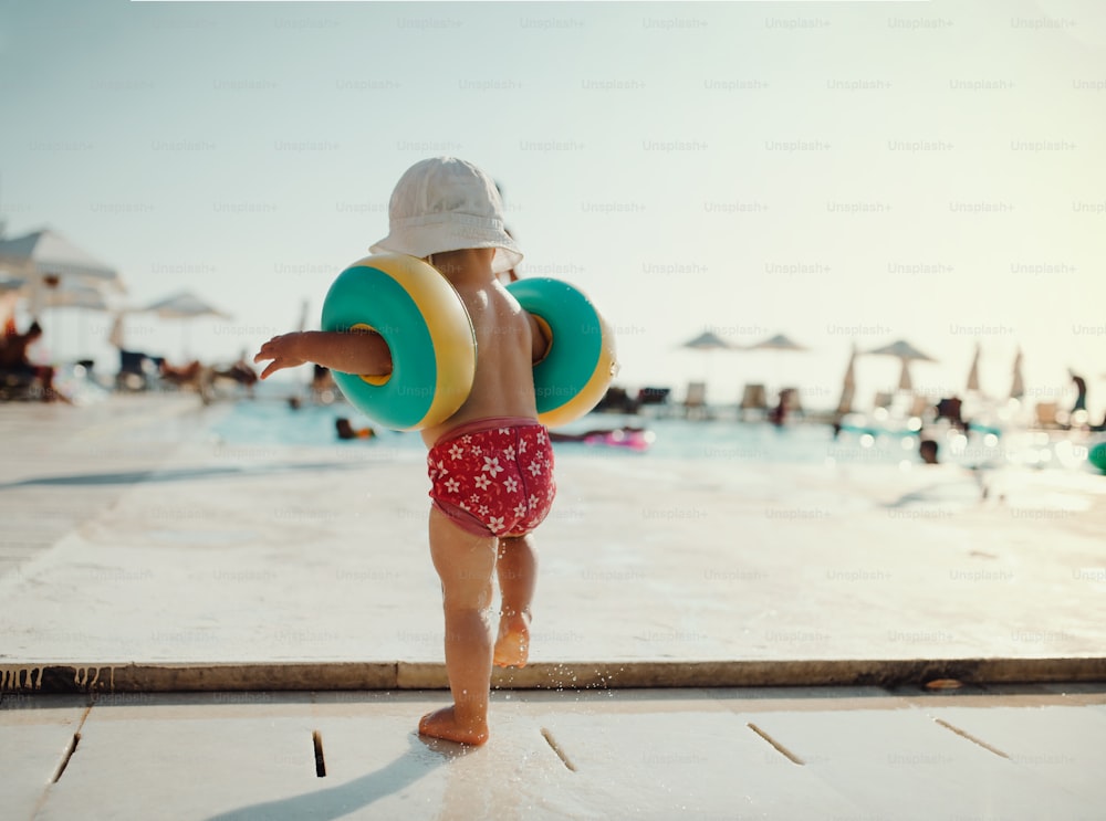 Una vista posteriore di un bambino piccolo con bracciali che cammina sulla spiaggia durante le vacanze estive.