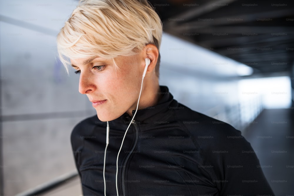 A portrait of young sportswoman with earphones doing exercise outdoors, resting.