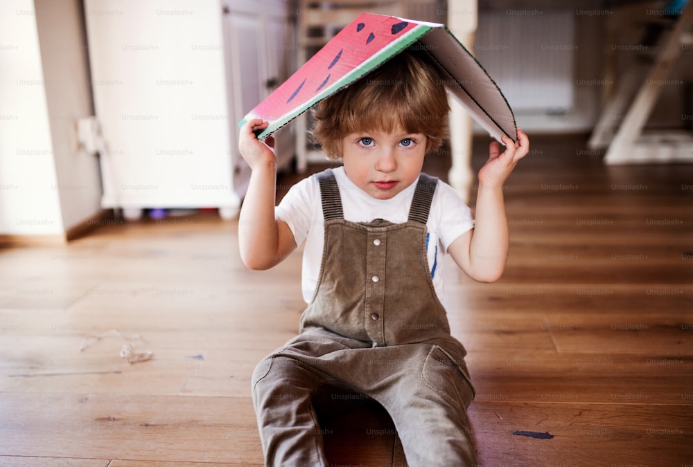 Un bambino che gioca con un grande frutto giocattolo all'interno di casa, guardando la macchina fotografica.
