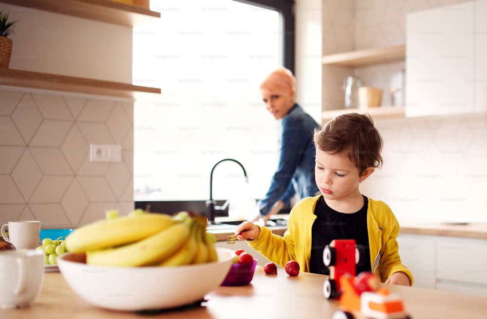 A happy young mother with small daughter eating fruit in a kitchen.