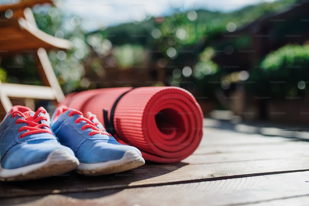 Composition of exercise mat and trainers outdoors on a terrace in summer.