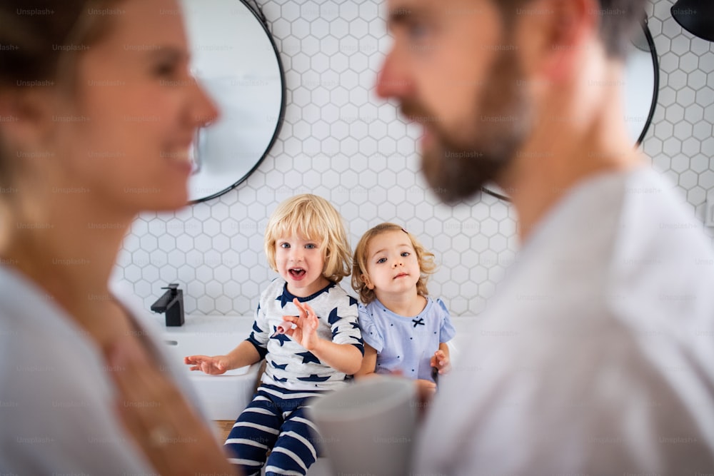 Une jeune famille avec deux jeunes enfants à l’intérieur dans la salle de bain, en train de parler.