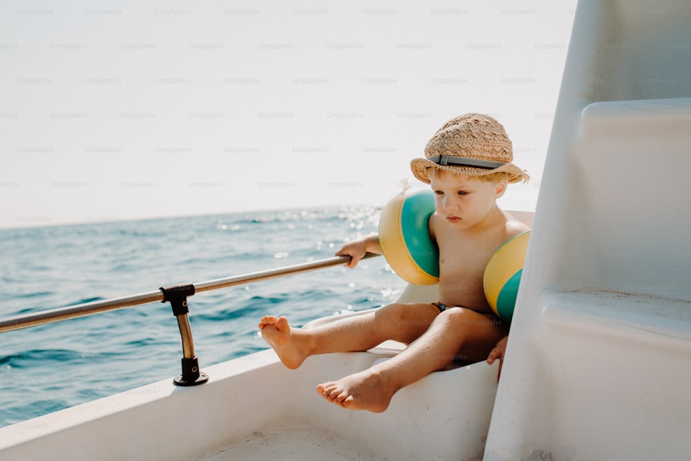 Un niño pequeño con brazaletes sentado en un barco de vacaciones de verano, sosteniendo una barandilla.