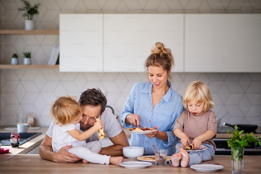 Vista frontale della giovane famiglia con due bambini piccoli all'interno in cucina, mangiando frittelle.