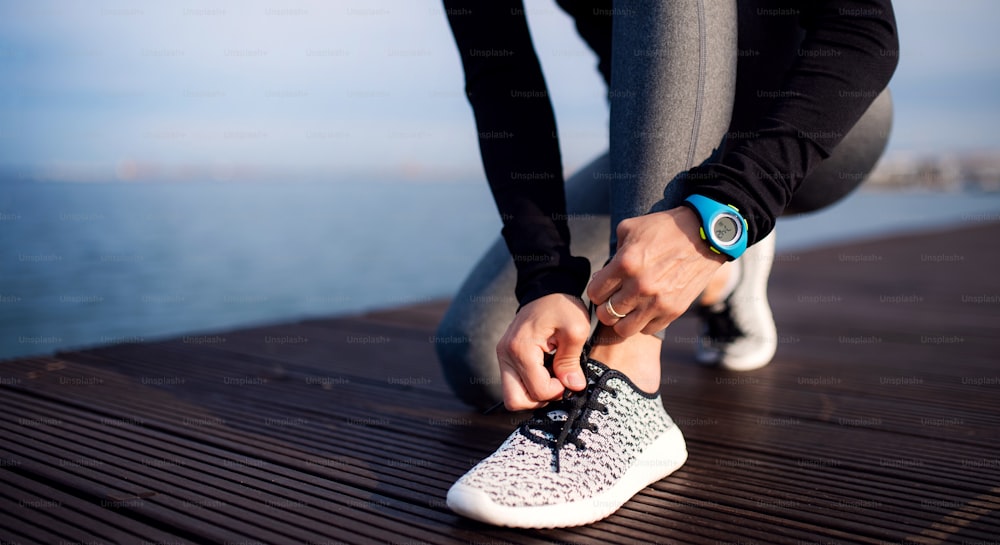 A midsection of young sportswoman with smartwatch outdoors on beach, tying shoelaces.