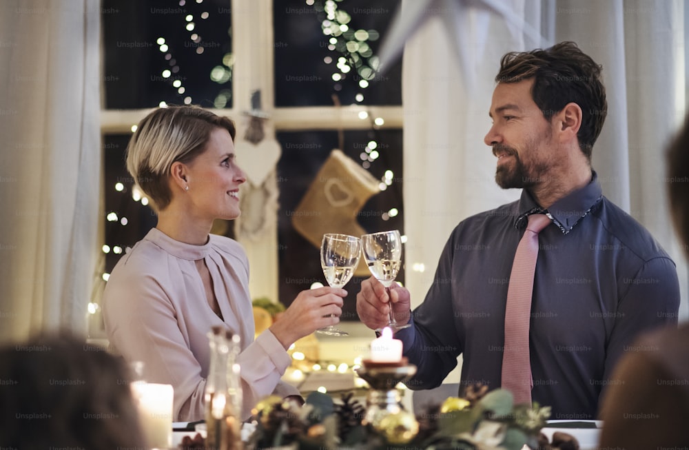 Front view portrait of happy couple indoors at the table celebrating Christmas, clinking glasses.