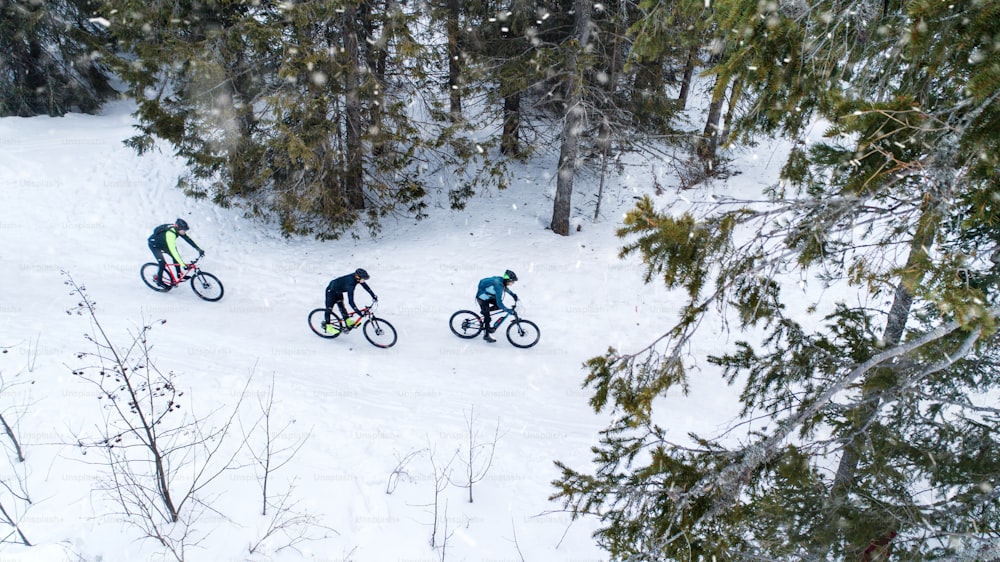 Veduta aerea di mountain biker che cavalcano su strada coperta di neve nella foresta all'aperto in inverno.