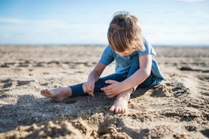 A barefoot small girl playing in sand outdoors on beach.