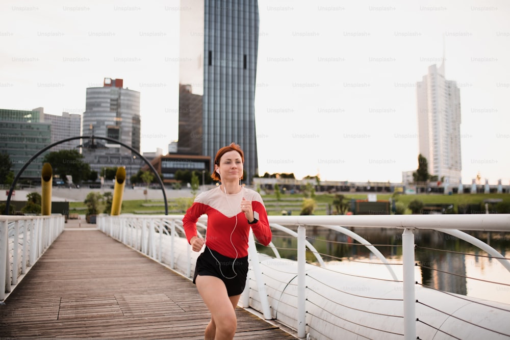 街で屋外をジョギングするイヤホンを付けた若い女性ランナーの正面図。