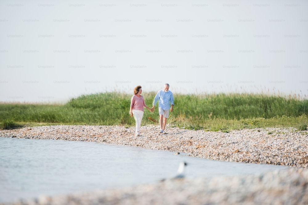 Una coppia di anziani in vacanza a piedi in riva al lago. Copia spazio.