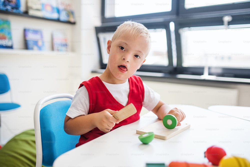 Um garoto feliz da escola com síndrome de Down sentado na mesa da sala de aula, aprendendo.