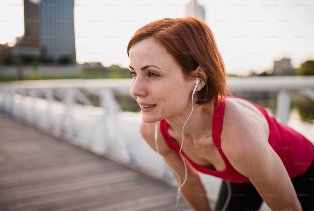 Young woman runner with earphones in city, resting on the bridge. Copy space.