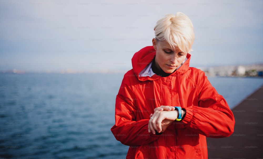 Eine junge Sportlerin, die draußen am Strand steht und eine Smartwatch benutzt. Speicherplatz kopieren.