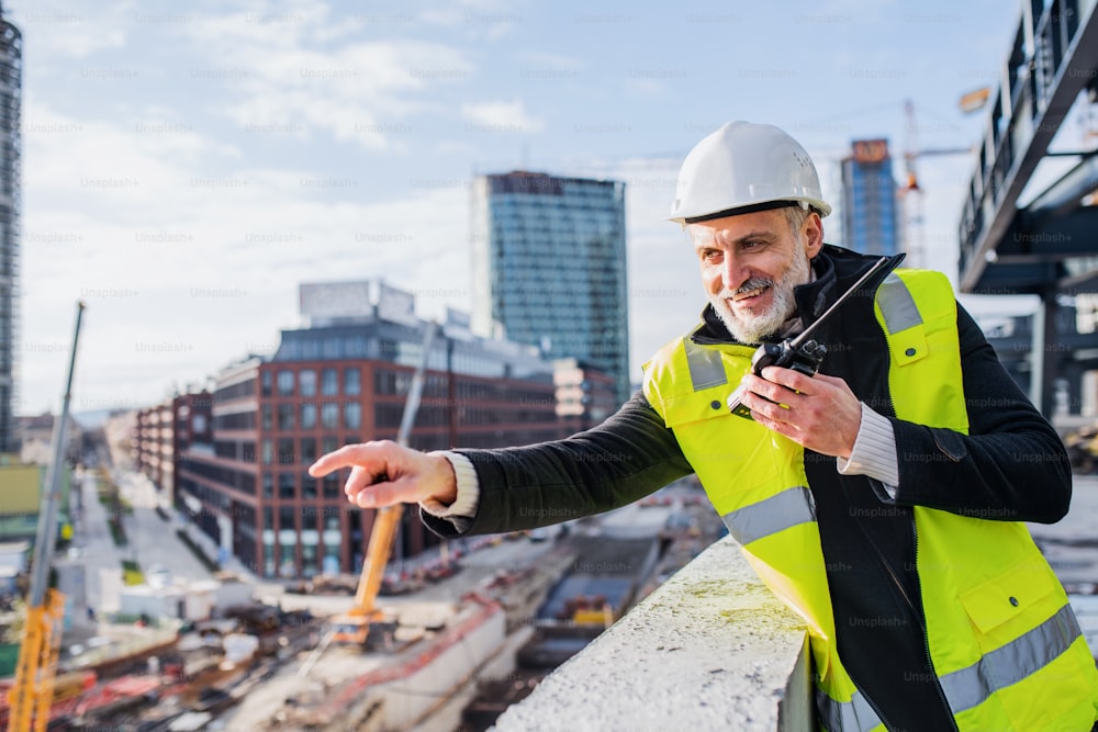 Ingeniero de hombre usando walkie talkie al aire libre en el sitio de construcción.