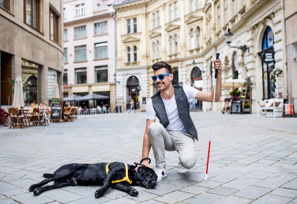 Un joven ciego con bastón blanco y perro guía en una zona peatonal de la ciudad.